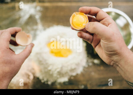 Pasta fatta in casa il processo di cottura, pasta di preparazione. Lo chef maschio mani con uovo, un mazzetto di farina a fontana sul tavolo di legno Foto Stock