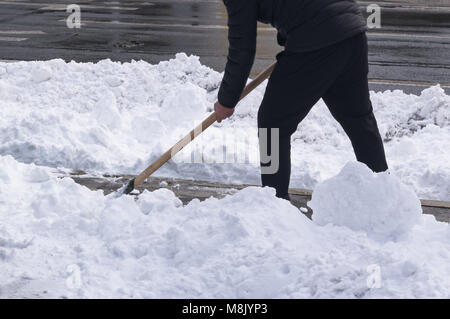 La pulizia della neve con una pala dopo una nevicata. Un uomo rimuove la neve su una strada di città Foto Stock