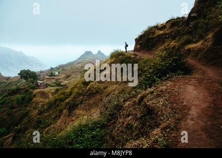 Escursionista silhouette guarda in valle e si ascolta il silenzio. La nebbia e la nebbia appendere sopra le cime della montagna sul sentiero per Pompas. Santo Antao Capo Verde Foto Stock