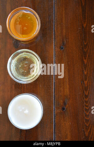 Tre tipi di miele in ciotole in vetro su sfondo di legno Foto Stock