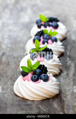 Mini Pavlova nidi di meringa con frutti di bosco e timo su tavola in legno rustico Foto Stock