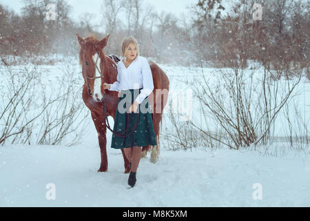 Bella donna è in piedi accanto a un cavallo in un parco d'inverno. Foto Stock