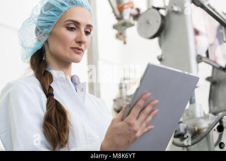 Donna esperto di analisi delle informazioni sul tablet durante il lavoro in fabbrica contemporanea Foto Stock