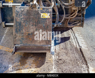 Lavoratore conducente minipala rimuovere indossato asfalto durante la riparazione di opere stradali Foto Stock