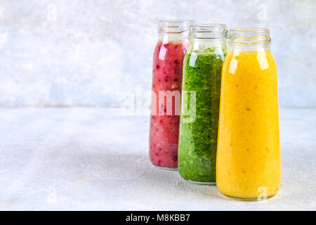 Verde, giallo, viola i frullati in bottiglie di bacche, verdi, arance su una lavagna bianca su una tabella di colore grigio Foto Stock