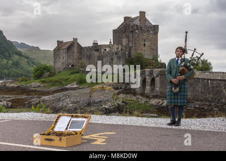 Dornie, Scozia - 10 giugno 2012: Lone suonatore di cornamusa in completo abito scozzese tradizionale di fronte a Brown-stone Eilean Donan Castle. Sotto pioggia-pesante Foto Stock