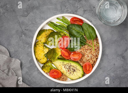 La dieta sana prima colazione. la quinoa e verdure: pomodori, asparagi, broccoli, avocado e spinaci, chia semi in una ciotola bianco sul cemento grigio bac Foto Stock