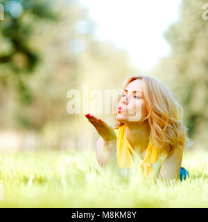 Giovane donna si brucia un bacio giacente su erba verde prato Foto Stock