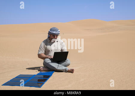 Un uomo lavora in remoto su un notebook accanto a un pannello solare portatile nel deserto, autosufficiente e sostenibilità in un ambiente remoto con spazio di copia Foto Stock