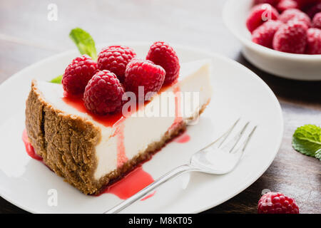 Cheesecake ai lamponi e salsa di frutti di bosco su piastra bianca, vista ingrandita, il fuoco selettivo. Fetta di torta al formaggio Foto Stock