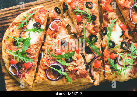 In casa flatbread pizza con salsa di pomodoro e olive nere, cipolla, mozzarella e rucola fresca sul tagliere di legno, vista dall'alto, tonica immagine Foto Stock