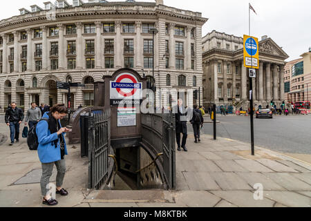 Una donna controllando il suo telefono al di fuori della Banca stazione di tubo di ingresso nella città di Londra Foto Stock