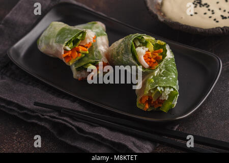 Fresca vegano fatti a mano asian involtini primavera con spaghetti di riso, avocado, carote e tahini medicazione sul piatto nero Foto Stock