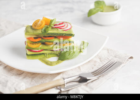 Materie zucchine lasagne con verdure e pesto, sfondo luminoso. Vegetariano crudo concetto di dieta. Foto Stock