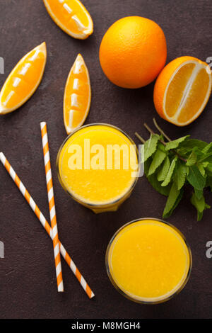 Due bicchieri di succo d'arancia appena spremuto e menta su un colore marrone scuro dello sfondo. Vista superiore Foto Stock