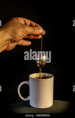 Mano d'uomo preparando il tè in una ciotola con infusore, sullo sfondo Foto Stock