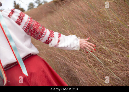 Celibe (può essere distinto da nastri) ragazza ucraina vestito in costumi tradizionali stroking erba mentre promenading nel campo Foto Stock