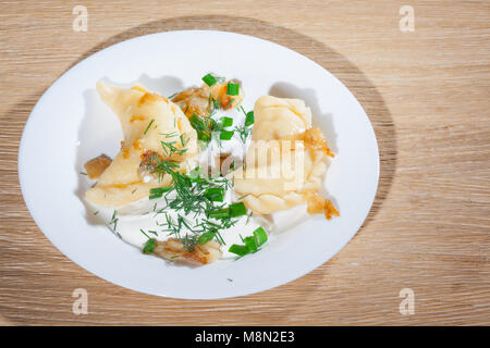 Vareniki ucraini servita sulla piastra Faror con cipolle, panna acida e aneto Foto Stock