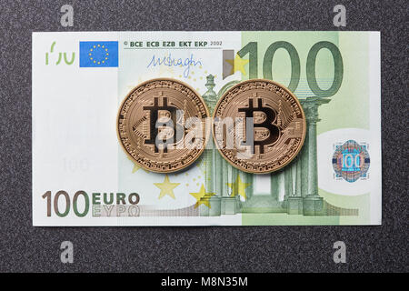 Le monete d'oro bitcoin e un centinaio di banconote in euro su sfondo scuro Foto Stock