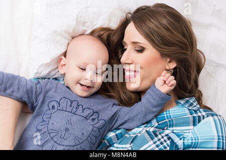 Felice madre e suo figlio bambino giacente su un letto insieme. La famiglia felice. La madre e il bambino neonato ritratto. Foto Stock