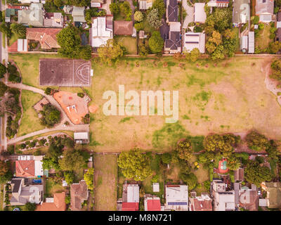 Guardando verso il basso in corrispondenza di tetti di case, di un parco giochi per bambini e parcheggio - paesaggio aerea della zona residenziale Foto Stock