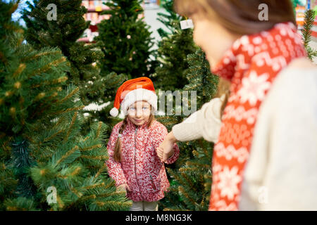 Angolo alto ritratto di carino bambina indossa Santa hat holding madri braccio mentre la scelta di abete al mercato in mall Foto Stock