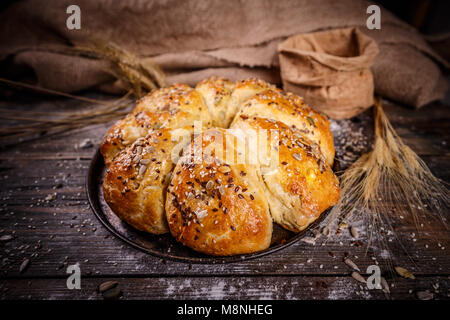 Appena sfornato il triangolo di frumento panini con semi su sfondo rustico Foto Stock