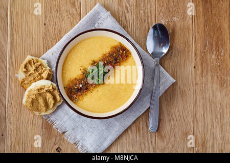 Viola ciotola di cremosa zuppa di zucca guarnito con aneto, servita con fette di pane ricoperte con Incolla su homespun igienico su sfondo rustico, Foto Stock