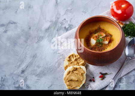 Pentola di creta di piccante cremosa zuppa di zucca guarnito con aneto, servita con pane tostato coperte con pasta e pomodoro rosso su bianco a trama, sfondo Foto Stock