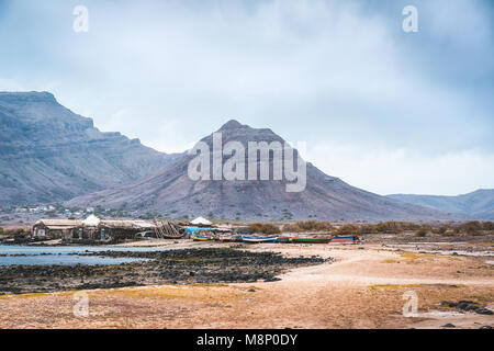 Misterioso paesaggio del litorale sabbioso con fisher village e il nero le montagne vulcaniche in background. Baia das Gatas. A nord di Calhau, Sao Vicente Isola Capo Verde Foto Stock