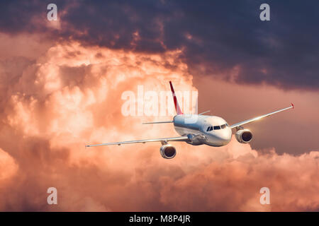 Bella aereo è volare in nuvole basse al tramonto colorato. In scena con bianco aereo passeggeri sky con l'arancione e il rosso nuvole. Gli aerei passeggeri. Foto Stock