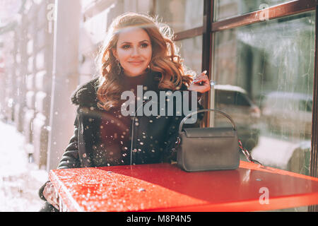 Sorridente Redhead donna in giacca nera in Street Cafe' all'aperto. Street style Foto Stock