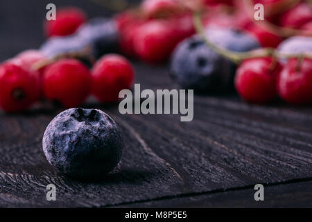 Frutti di bosco surgelati mirtillo i mirtilli in una brina su un tavolo di legno closeup contro uno sfondo di rosso di bacche Ribes in una sfocatura sullo sfondo Foto Stock