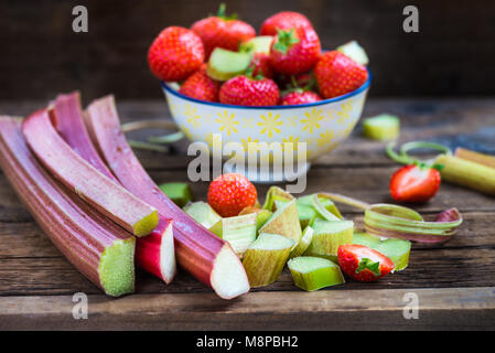Pezzi di materie e fresche tagliate il rabarbaro e le fragole scuro su sfondo rustico Foto Stock