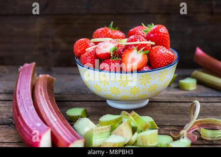 Pezzi di materie e fresche tagliate il rabarbaro e le fragole scuro su sfondo rustico Foto Stock