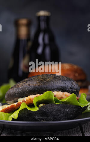 Cucinata fresca hamburger con rotolo di colore nero, verdure e salmone cotoletta. Sandwich fatti in casa da vicino Foto Stock