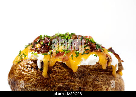 Vista laterale di un carico di patate al forno con erba cipollina, bacon, formaggio cheddar, panna acida su bianco Foto Stock
