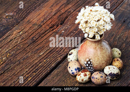 Uova di quaglia e fiori secchi nel vaso piccolo sul vecchio tavolo in legno, vista dall'alto. Pasqua in stile vintage (fuoco selettivo). Foto Stock