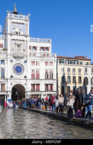 I turisti a piedi su passerelles di fronte alla Torre dell Orologio attraverso un invaso Piazza San Marco, Piazza San Marco, Venezia, Italia durante l'Acqua Alta hig Foto Stock