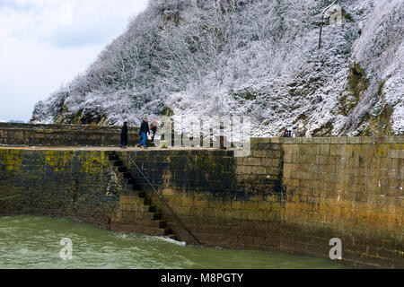 18/03/2018 Charlestown, Cornwall, Regno Unito, Editoriale: Sconosciuto i membri del pubblico a piedi lungo la parete del porto a Charlestown con coperta di neve scogliere Foto Stock
