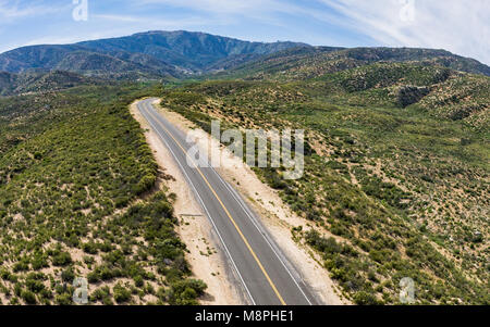 Grigio su strada in salita conduce attraverso le ondulate colline verdi sul bordo delle montagne. Foto Stock