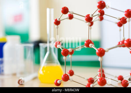 Vetreria chimica con liquido di formula e struttura molecolare modello presso la scienza in aula banco da laboratorio. Foto Stock