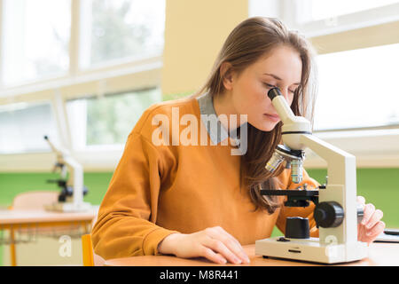 Alta scuola studentessa in biologia classe. Studente utilizzando microscopio per esaminare campioni. Foto Stock