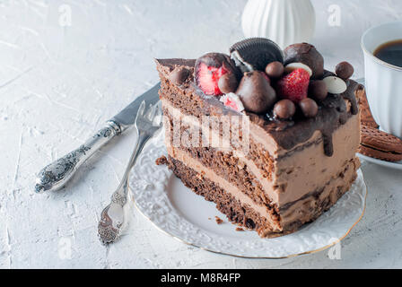 Pezzo di torta al cioccolato sulla piastra bianca, una tazza di caffè nero, brocca e biscotti al cioccolato su sfondo bianco. Vista superiore, copia dello spazio. Foto Stock