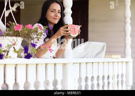 Ragazza giovane sulla veranda della casa di mangiare anguria dolce Foto Stock