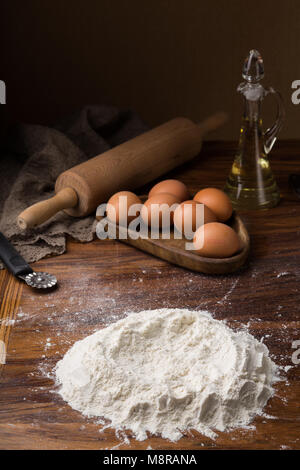 Flourpot, uova, mattarello, olio d'oliva in un recipiente su un sfondo di legno. Foto Stock
