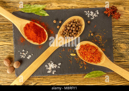 Composizione di spezie. Condimenti sul tavolo della cucina. Scheda di ardesia e cucchiai di legno. La vista dall'alto. Immagine luminosa. Foto Stock