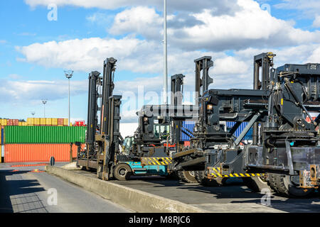 Una fila di Reach Stacker e gestore di camion parcheggiato sul contenitore di piattaforma di storage del terminal intermodale di un porto fluviale con contenitori in Foto Stock