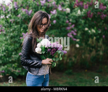 Giovane donna holding mazzetto di fiori mentre in piedi contro piante fiorite in posizione di parcheggio Foto Stock