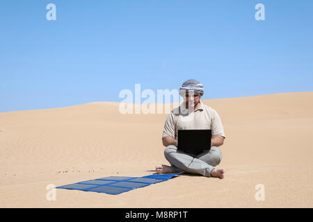 Uomo che lavora con un laptop che si ricarica da un pannello solare portatile all'aperto nel deserto. Lavorare in remoto con gadget, autosufficienza e spazio di copia ecocompatibile Foto Stock